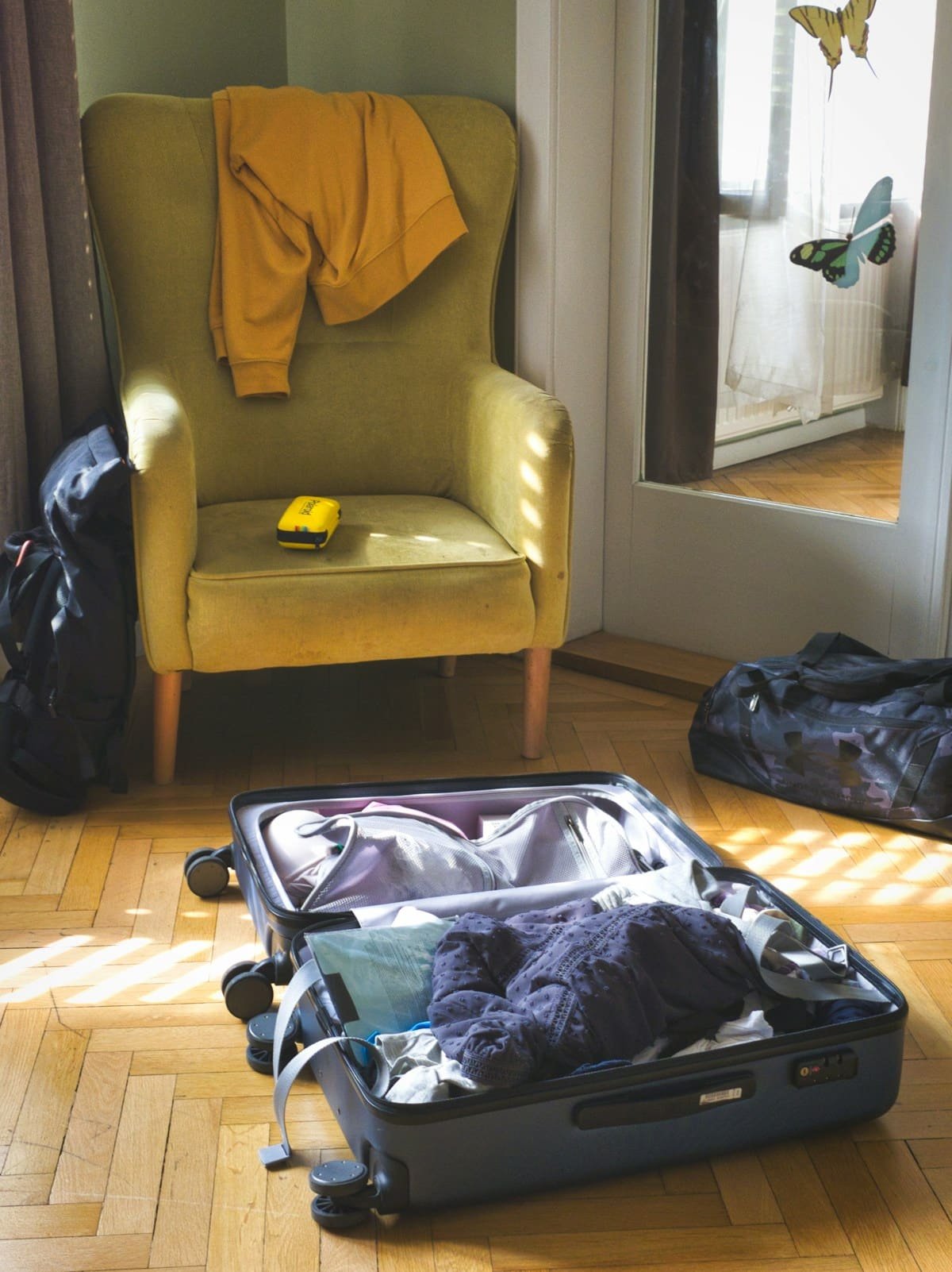 Geöffneter Reisekoffer mit Kleidung neben einem Sessel in einem hellen Zimmer