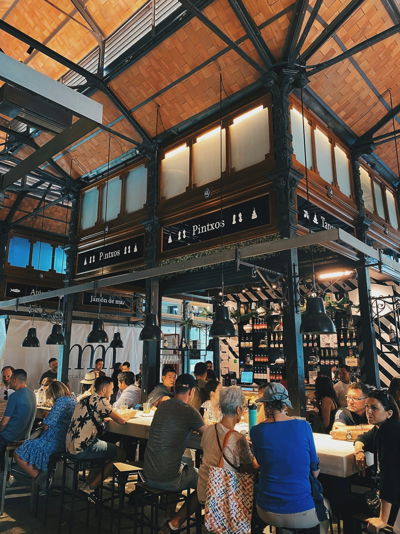 Menschen an Tischen im Mercado de San Miguel in Madrid, einer bekannten Markthalle für Tapas und regionale Spezialitäten